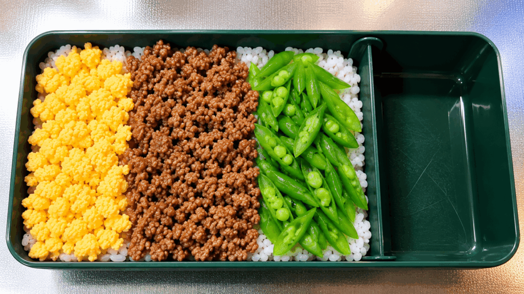 そぼろ弁当のごはんの上に肉・野菜・卵を並べた詰め方